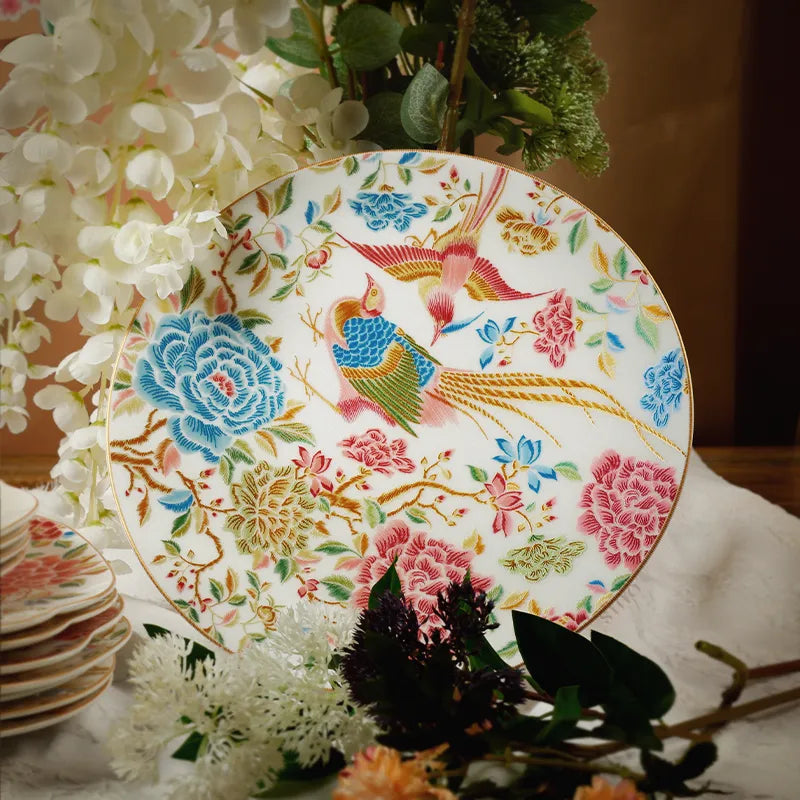 Bone china round dinner plate with floral and bird design, upright with flower decor background.