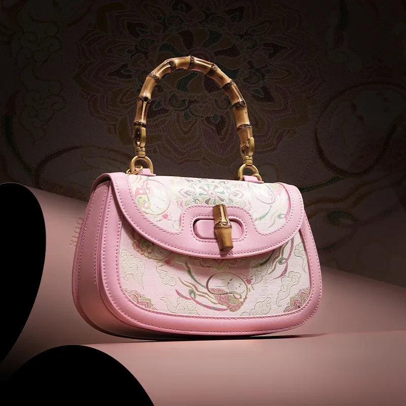 Pink Song brocade handbag displayed on pink leather, emphasizing its luxurious texture and bamboo handle.