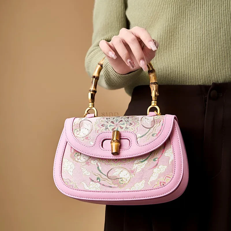 Model holding the pink Song brocade handbag with a bamboo handle, demonstrating its elegant carry style.