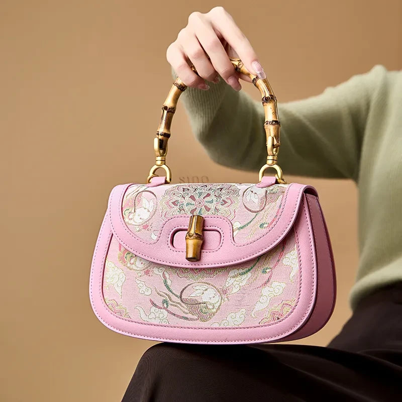 Model seated with the pink Song brocade handbag resting on her lap, showcasing its compact size and bamboo handle.