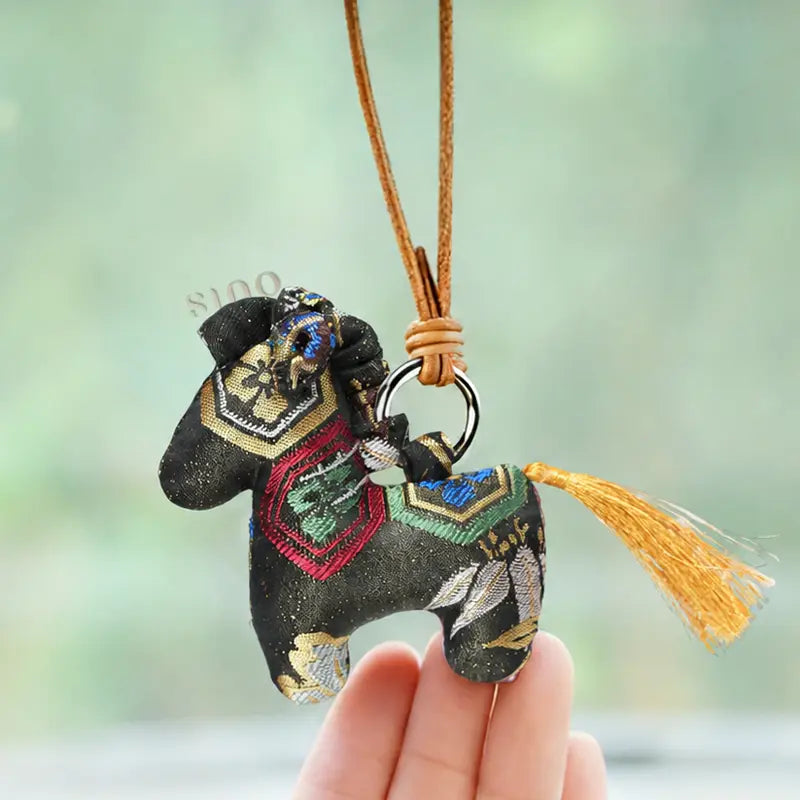 Auspicious handmade black Yunjin brocade horse bag charm shown by hand with colorful woven motifs, a leather cord, and a golden tail tassel.