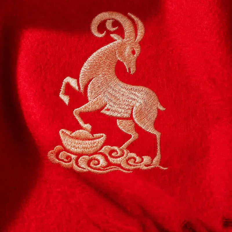 Close-up of a bright red cashmere scarf featuring intricate gold goat embroidery above an auspicious gold ingot motif.