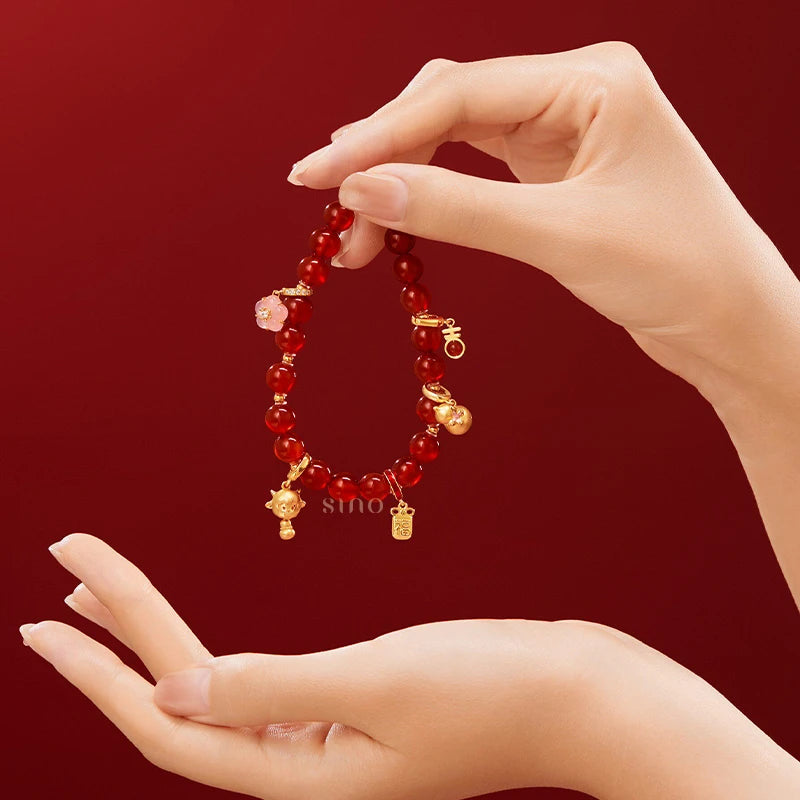 Red agate lucky bracelet held in the hand, featuring gold-tone charms and a pink floral pendant, an elegant Chinese New Year gift inspired by traditional Chinese symbolism.