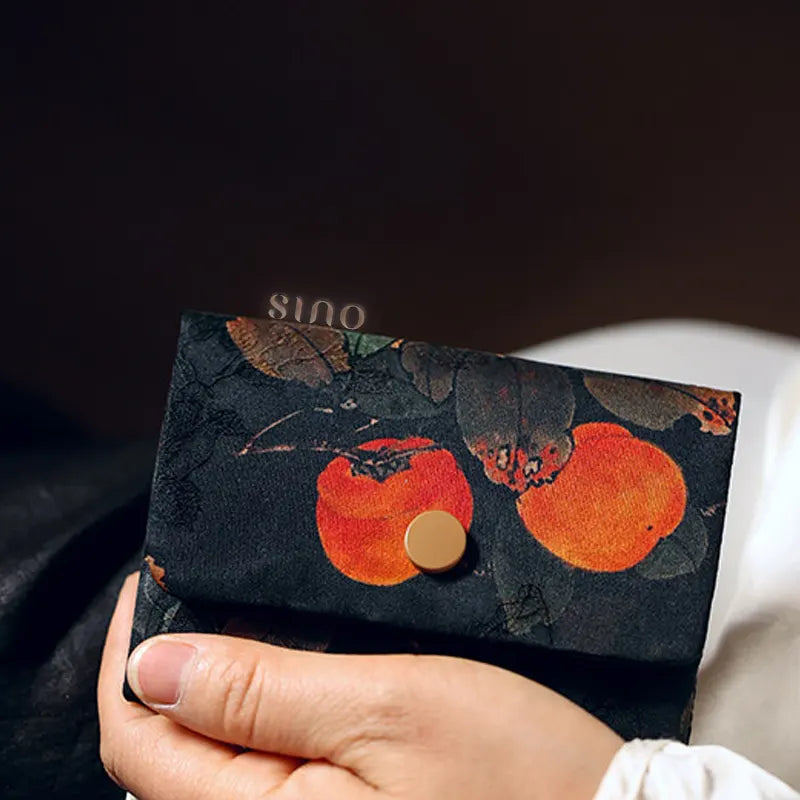 Handheld lifestyle view of the Chinese Xiangyunsha Silk Auspicious Persimmon Card Holder Wallet, highlighting its compact shape and symbolic persimmon design.