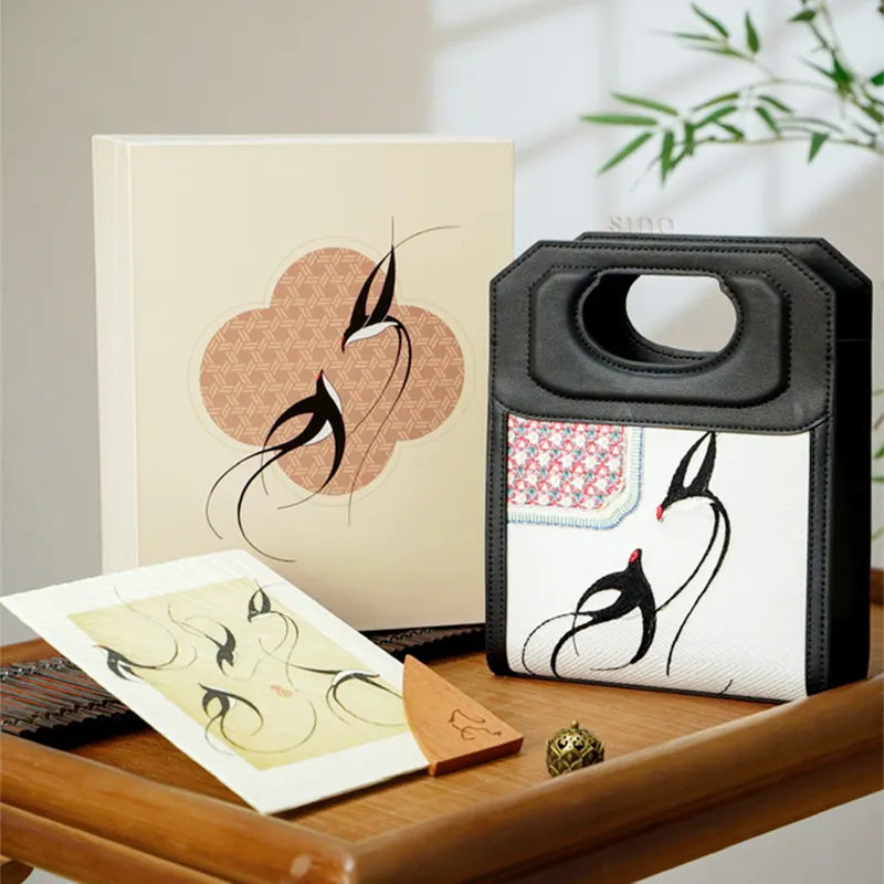 Handbag displayed on wooden table with matching gift box and stationery.