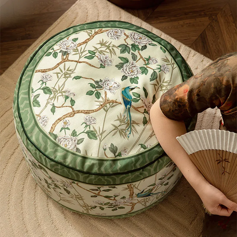 Model resting an elbow on the chinoiserie jade green couch cushion pouf beside a sofa.