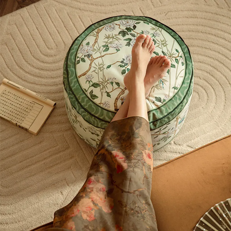 Top-down view of a model on a sofa with both feet resting on the chinoiserie jade green couch cushion pouf.