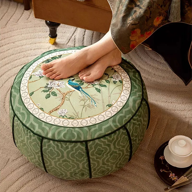 Chinoiserie jade green rest floor pouf used as a footrest in front of a sofa, with a model resting their feet on it in an angled top-down view.