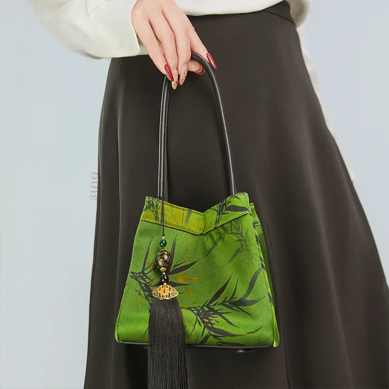 Model standing left-facing and holding the top handle, showing the front of the bucket bag.