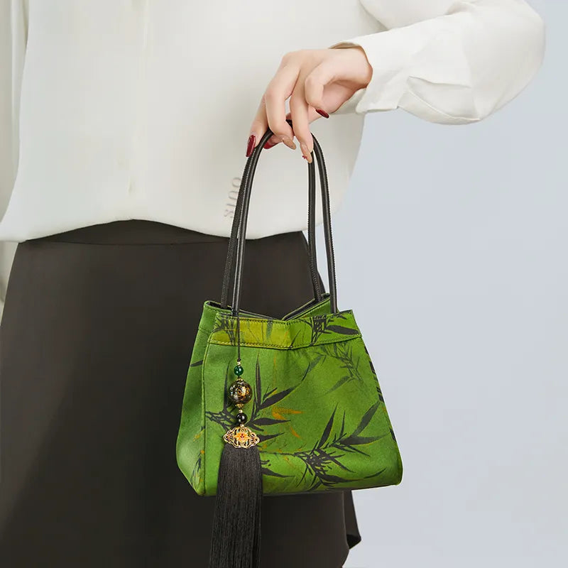 Model standing right-facing and holding the top handle, showing the front of the bucket bag.