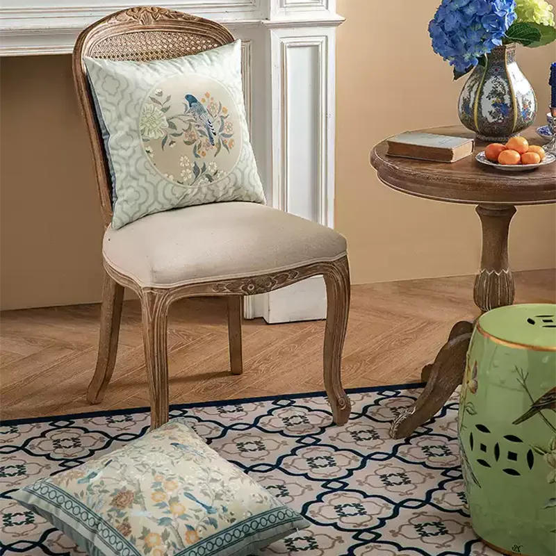 Chinoiserie luxury floral birds pillow on chair with another on floor.