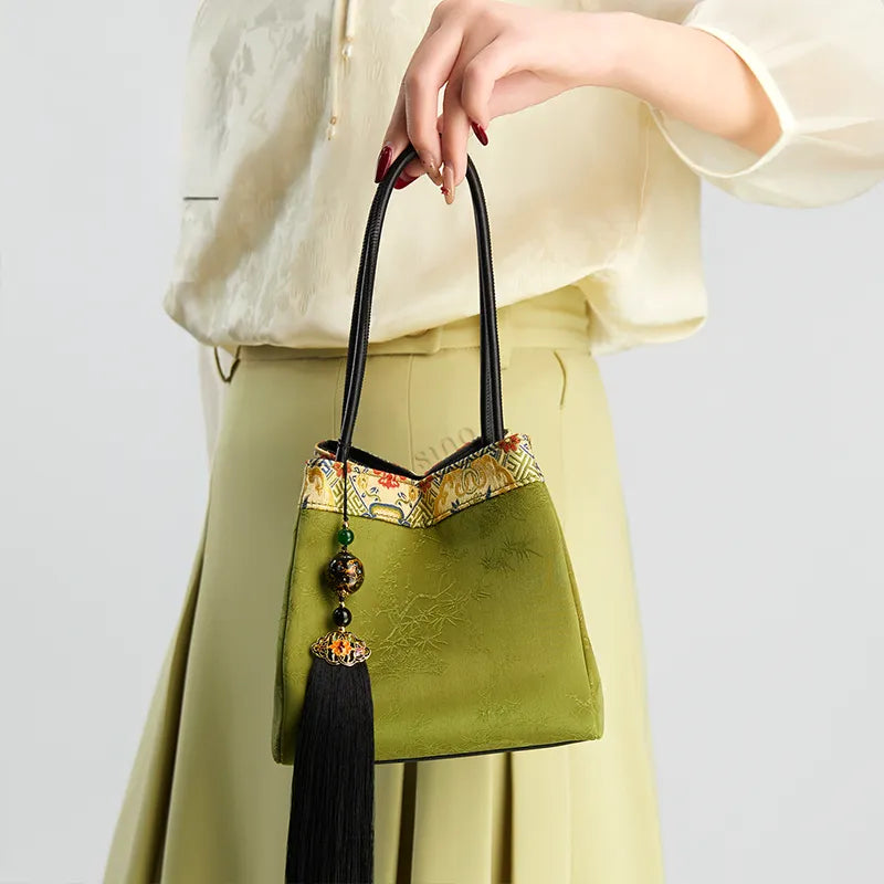Model standing right-facing and holding the top handle, showing the front of the bucket handbag.