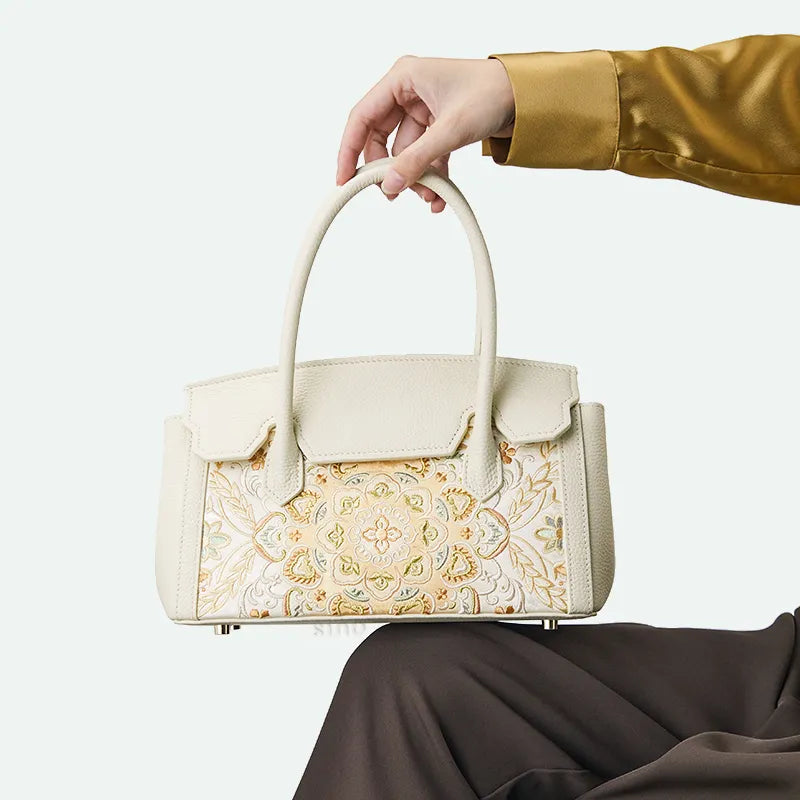 Model sitting with chinoiserie lotus motif leather handbag on knee.