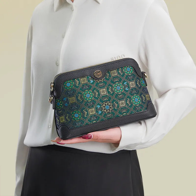 Model standing sideways holding the Lotus & Bat Motif clutch bag by hand.