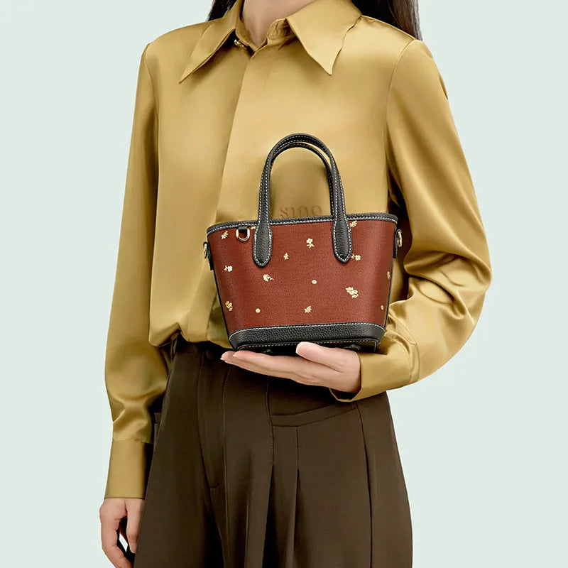 Model standing front-facing holding Chinoiserie Luxury Xiangyunsha Silk Leather Handbag with Printed Blossom.