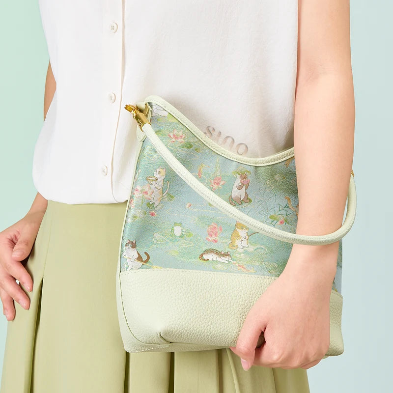 Model holding the Chinoiserie Springtime Tales leather shoulder bag with a charming cat and lotus design.