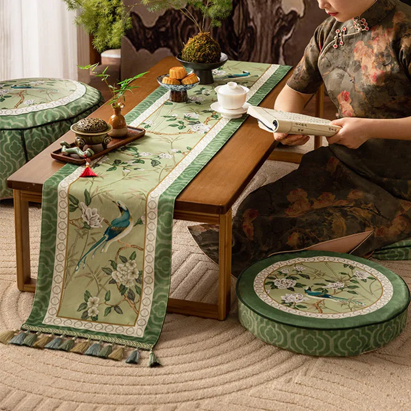 Chinoiserie vintage jade green long table runner with tassel fringe on a table with Chinese tea snacks and tea bowls, with a model reading a Chinese book beside it.