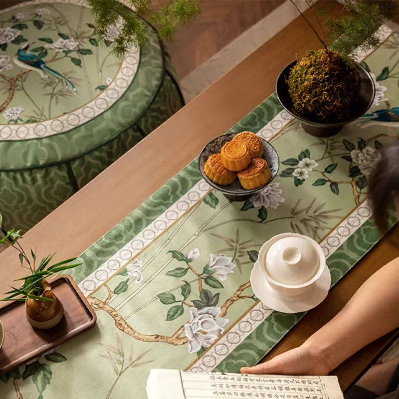 Top-down view of the jade green chinoiserie table runner with Chinese pastries on top, with a model reading a Chinese book nearby.