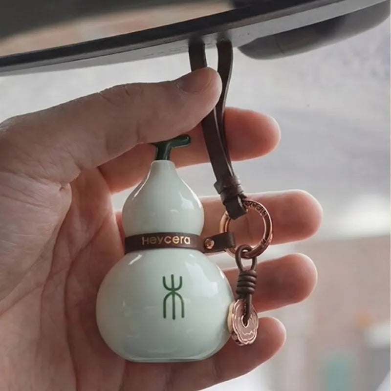 Handheld light green Wood element porcelain Hulu bag charm showing its glossy gourd shape, leather strap, and metal key ring.