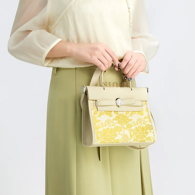 Model holding the gold woven Nanjing Brocade top handle bag with an elegant outfit.