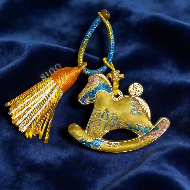 Auspicious gold Yunjin brocade rocking horse bag charm displayed on dark blue fabric with a colorful hanging cord and tassel.