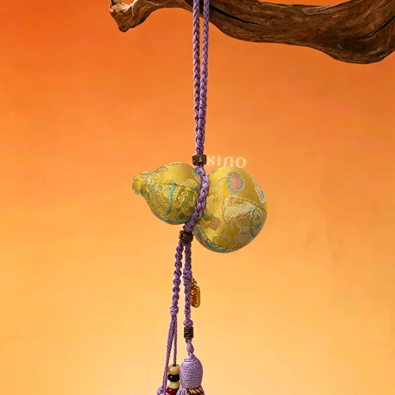 Golden Nanjing Yunjin brocade Hulu long tassel bag charm hanging against an orange background with a braided purple cord and decorative tassel.