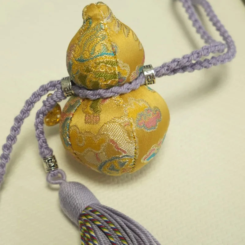 Close-up of the golden Yunjin brocade Hulu charm, showing the woven fabric, rounded double-gourd shape, purple cord, and tassel details.