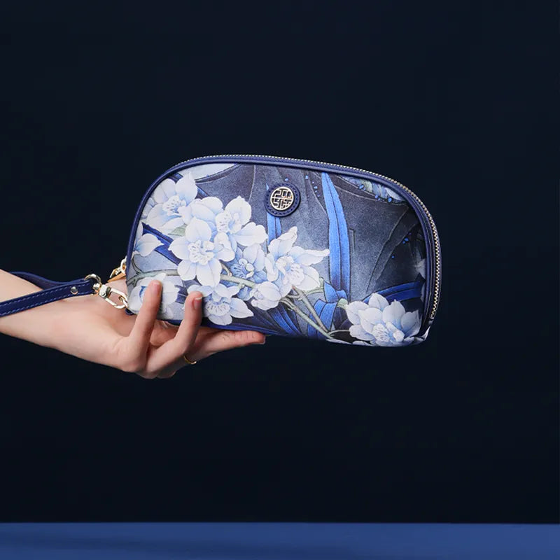 Hand Holding Chinoiserie Blue Orchid Clutch Against Blue Background.