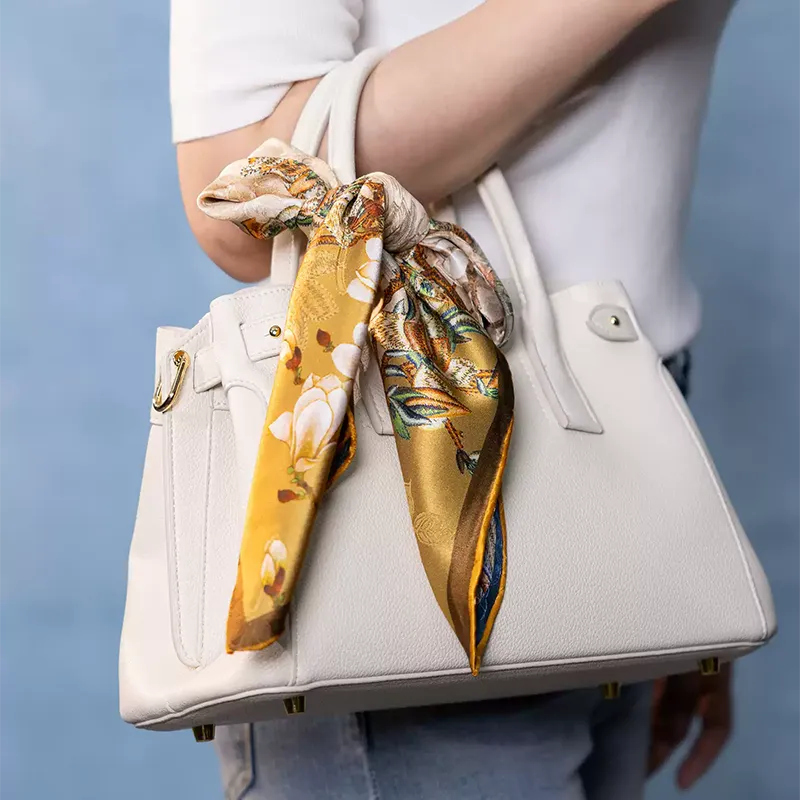 Luxury Nanjing Brocade Bloom silk square scarf tied on a white handbag, showing gold floral print and elegant gift styling.