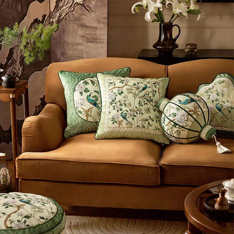 Square, lantern, and backrest luxury chinoiserie jade green decorative throw pillows leaning against each other on a sofa.