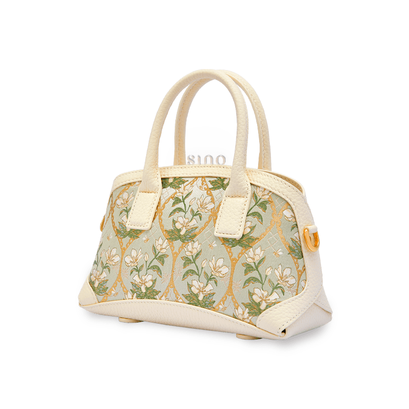 Angled view of the Dayun Brocade Verdant Floral leather top handle bag with a structured ivory silhouette.
