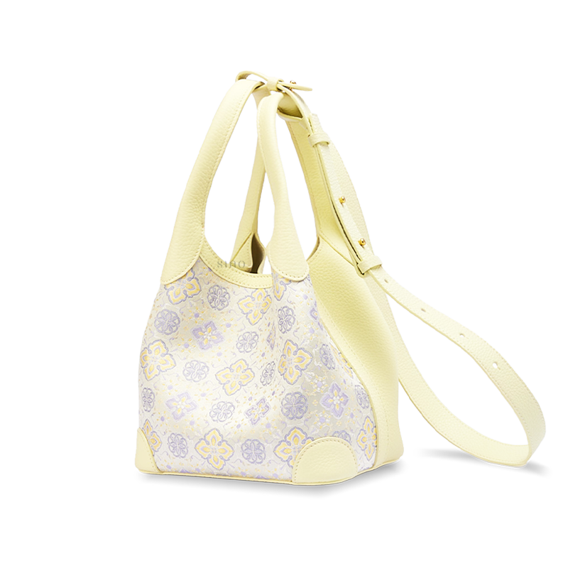 Angled view of the Luxury Shu Brocade Persimmon Calyx Motif Basket Tote Bag with long strap, showing the yellow leather trim and woven floral geometric design.
