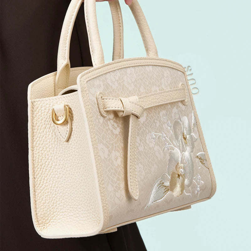 Model carrying the Luxury Shuanglin Silk Orchid Butterfly Embroidered Leather Top Handle Bag by hand, highlighting the embroidered leather design in a lifestyle setting.