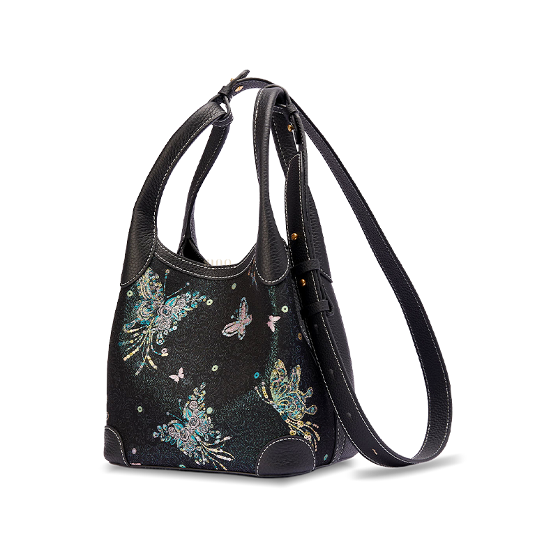 Angled view of the Luxury Song Brocade Butterfly & Pearl Leather Basket Tote Bag with adjustable long strap, showing the black leather side panel and woven butterfly brocade pattern.