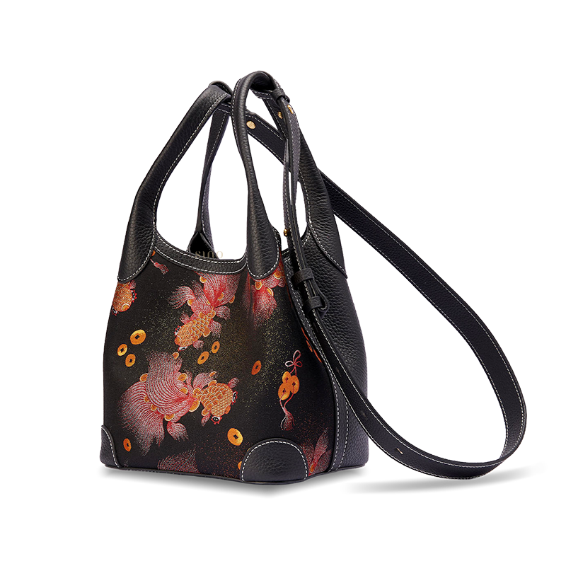 Angled view of the Song Brocade Golden Carp Leather Basket Tote Bag with adjustable long strap, showing the black leather side panel and woven carp design.