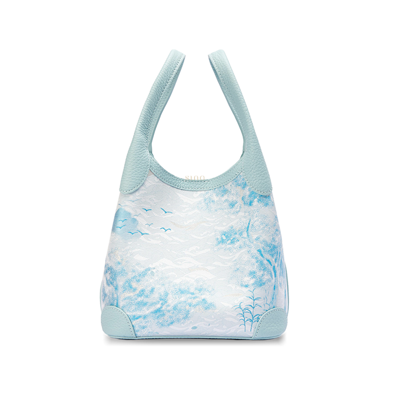 Front view of the Luxury Song Brocade Misty Mountain Forest Leather Basket Tote Bag, featuring a pale blue leather trim and a woven misty mountain landscape with forest and bird motifs.