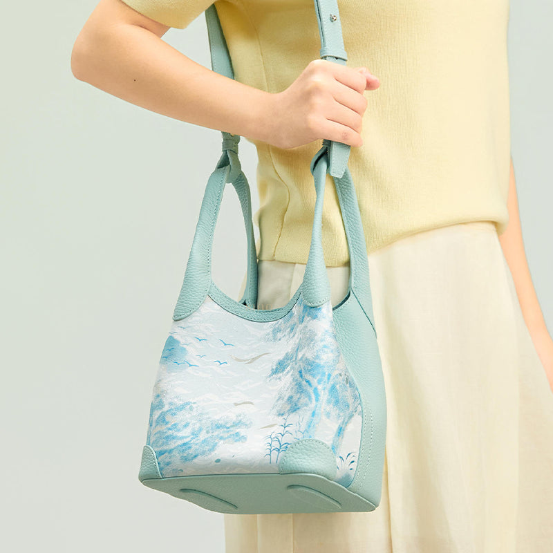 Model carrying the Luxury Song Brocade Misty Mountain Forest Leather Basket Tote Bag, showing the soft basket tote shape, pale blue leather trim, and scenic brocade pattern.