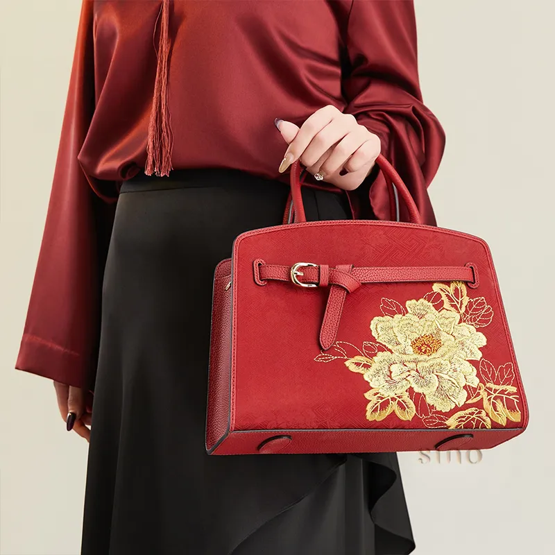 Model holding the red peony embroidered Xiangyunsha leather top handle bag in an elegant outfit.