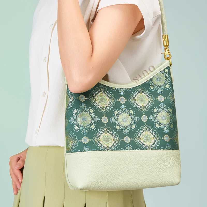 Side view of a model carrying the Chinoiserie Emerald Blossom leather shoulder bag under the arm.