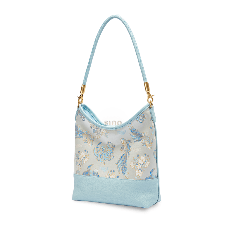 Angled view of a Chinoiserie Golden Jade Romance shoulder bag crafted from Shu Brocade and light blue leather.