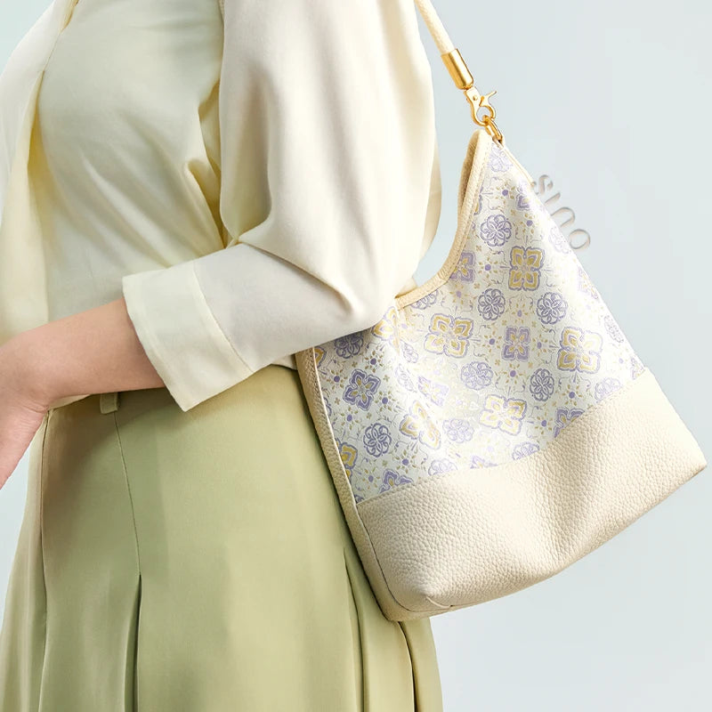 Side view of a model carrying the Chinoiserie Persimmon Calyx leather shoulder bag under the arm.