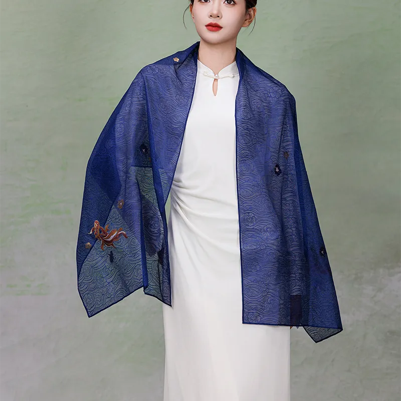 Model wearing a deep blue Nanjing Yunjin brocade silk shawl open across both shoulders, displaying flowing woven patterns and delicate gold-thread accents.