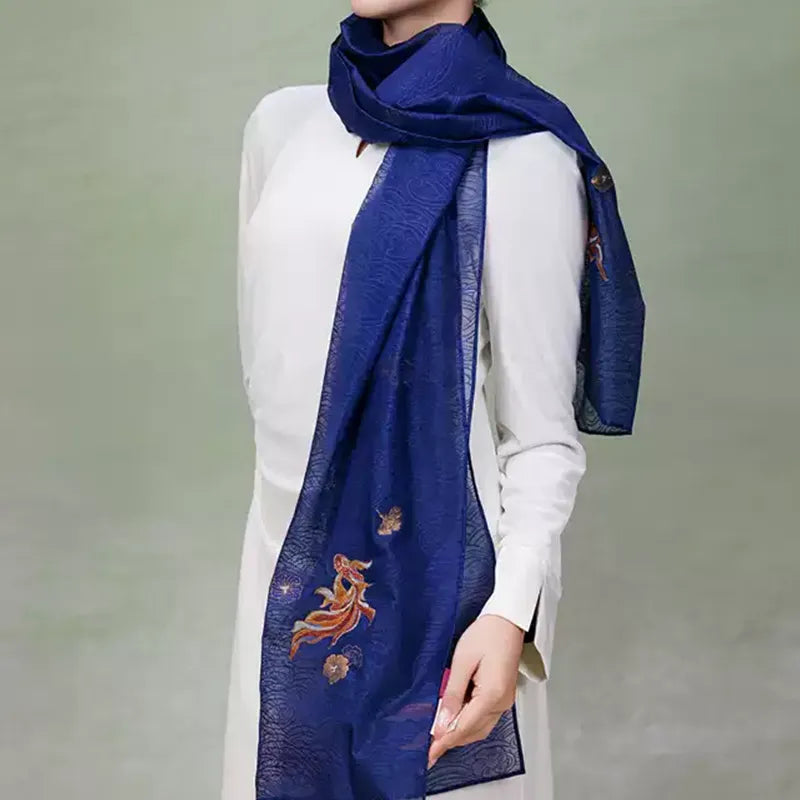 Deep blue Nanjing Yunjin mulberry silk shawl wrapped loosely around the neck, with one long end displaying the traditional fish and floral pattern.