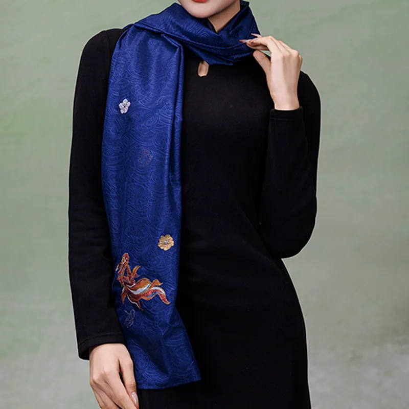 Handcrafted blue Nanjing Yunjin mulberry silk shawl wrapped around the neck over a black dress, with a decorative fish motif on the hanging end.