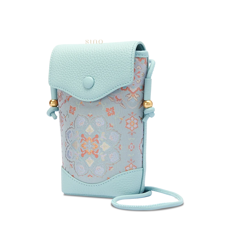 Light blue Song Brocade phone bucket bag for women with Baoxiang floral pattern and leather details, angled front view.