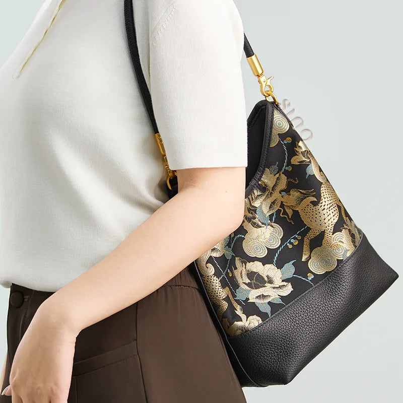 Side view of a model carrying the Black Gold Qilin Peony leather shoulder bag under the arm.