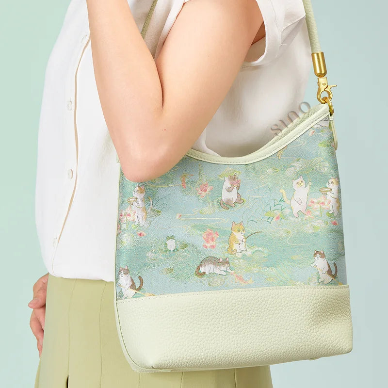 Side view of a model carrying the pale green Springtime Tales shoulder bag featuring playful cats and lotus flowers.