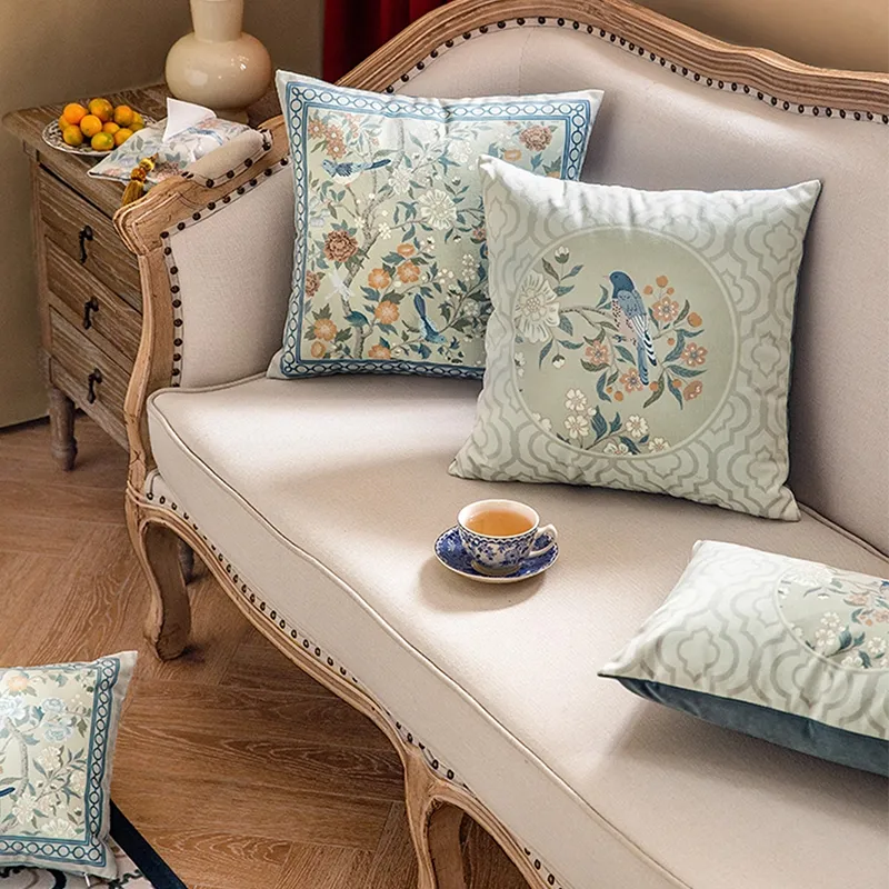 Three chinoiserie luxury floral birds pillows on sofa, side view.
