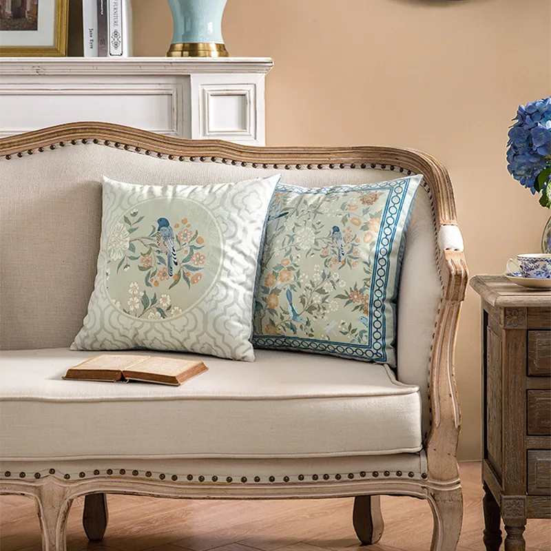 Two chinoiserie luxury floral birds pillows on sofa, front view.