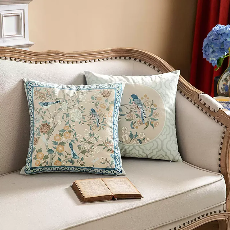 Two chinoiserie luxury floral birds pillows on sofa, angled view.